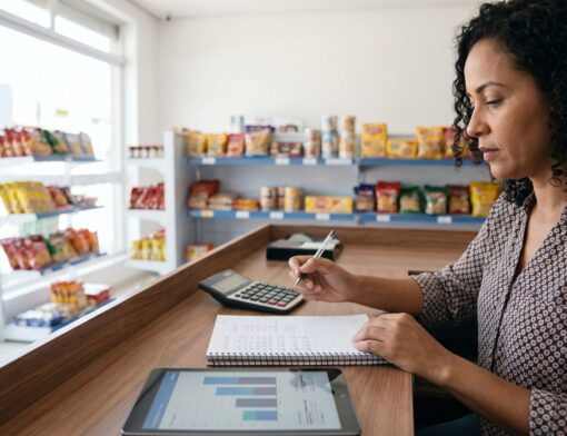 Comerciante revisando as contas da loja com calculadora, caderno e tablet com gráfico